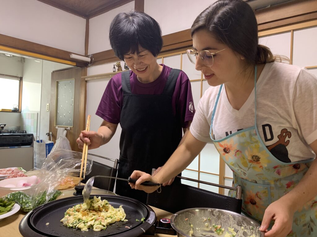 Japanese cooking class. Student pouring okonomiyaki on hot pan.