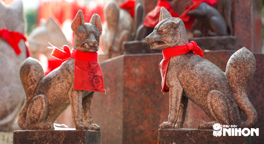 Två japanska kitsune-statyer med röda haklappar/förkläden.