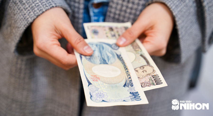 Person som håller i 10,000 yen och 1,000 yen sedlar