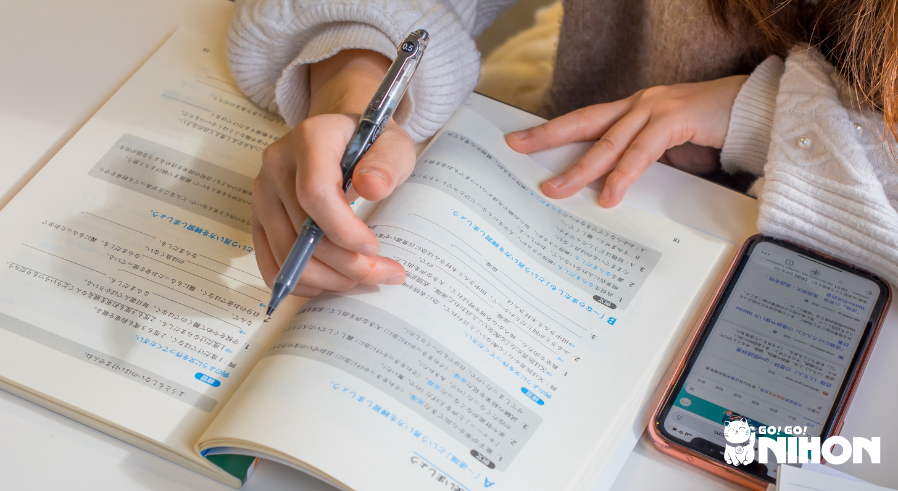 Une personne tenant un stylo par-dessus un manuel du JLPT N4 près d'un téléphone.