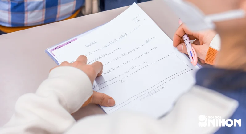 En elev som sitter vid ett skrivbord med en rosa penna i handen och läser på ett arbetsblad i japanska