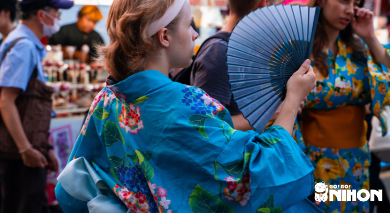 Person in blue kimono holding fan at obon festival
