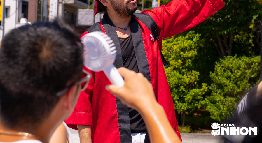 A hot and sweaty man trying to cool down with a portable fan while listening to a Tour Leader
