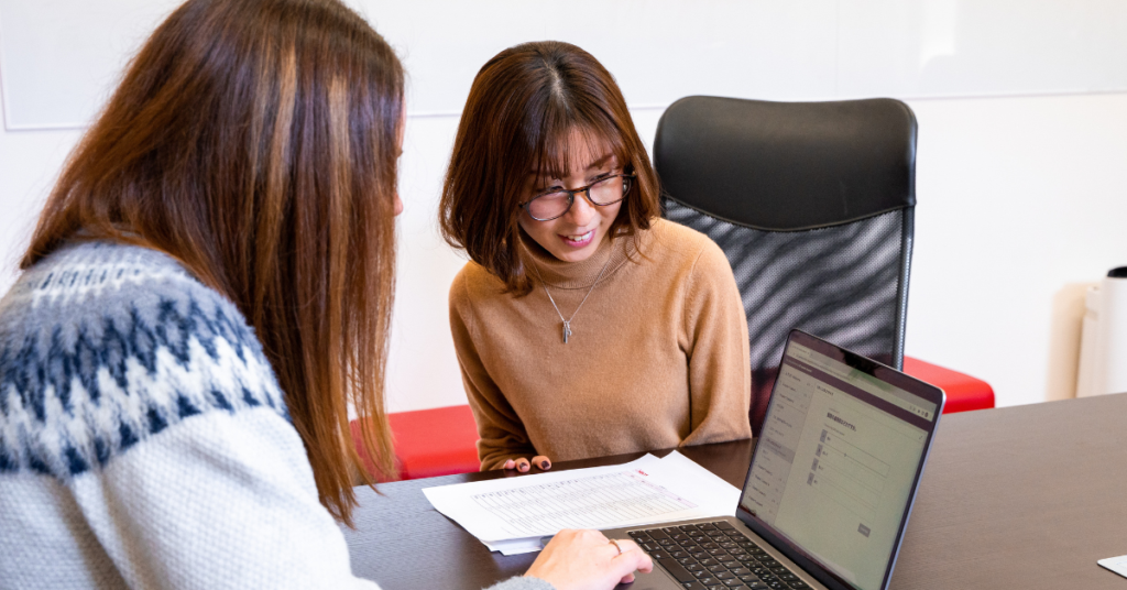 two people at a desk looking at a laptop together